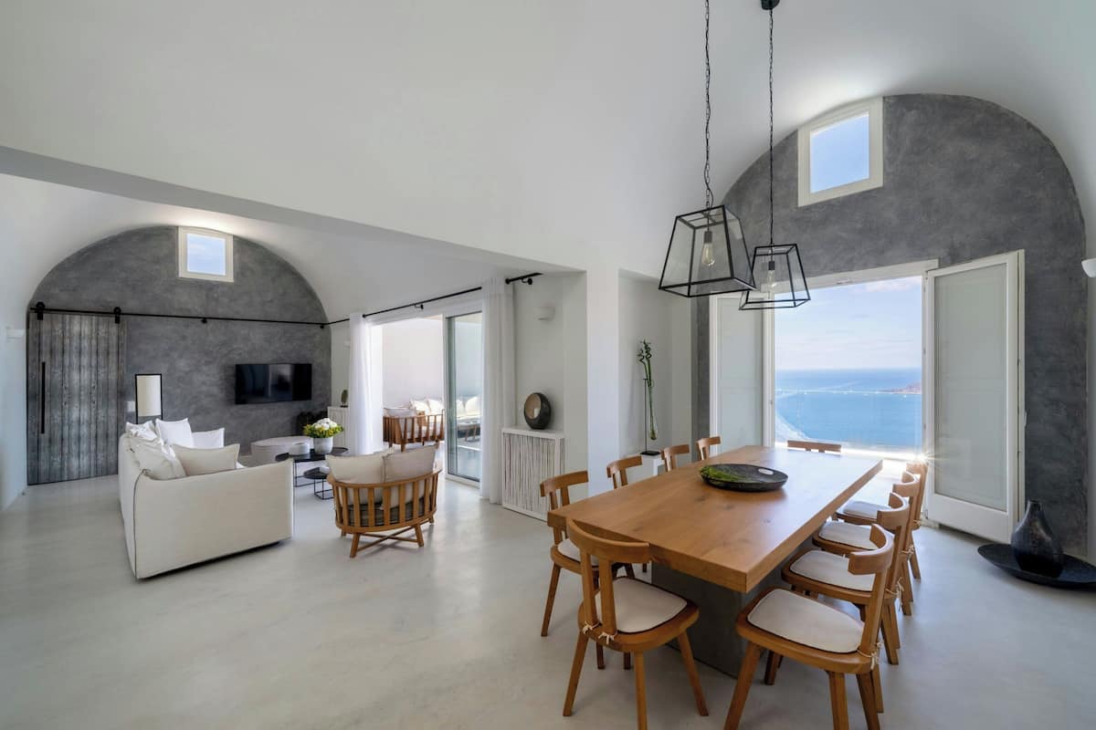 A spacious living area with a large wooden dining table, a sofa, and a TV mounted on a curved wall.