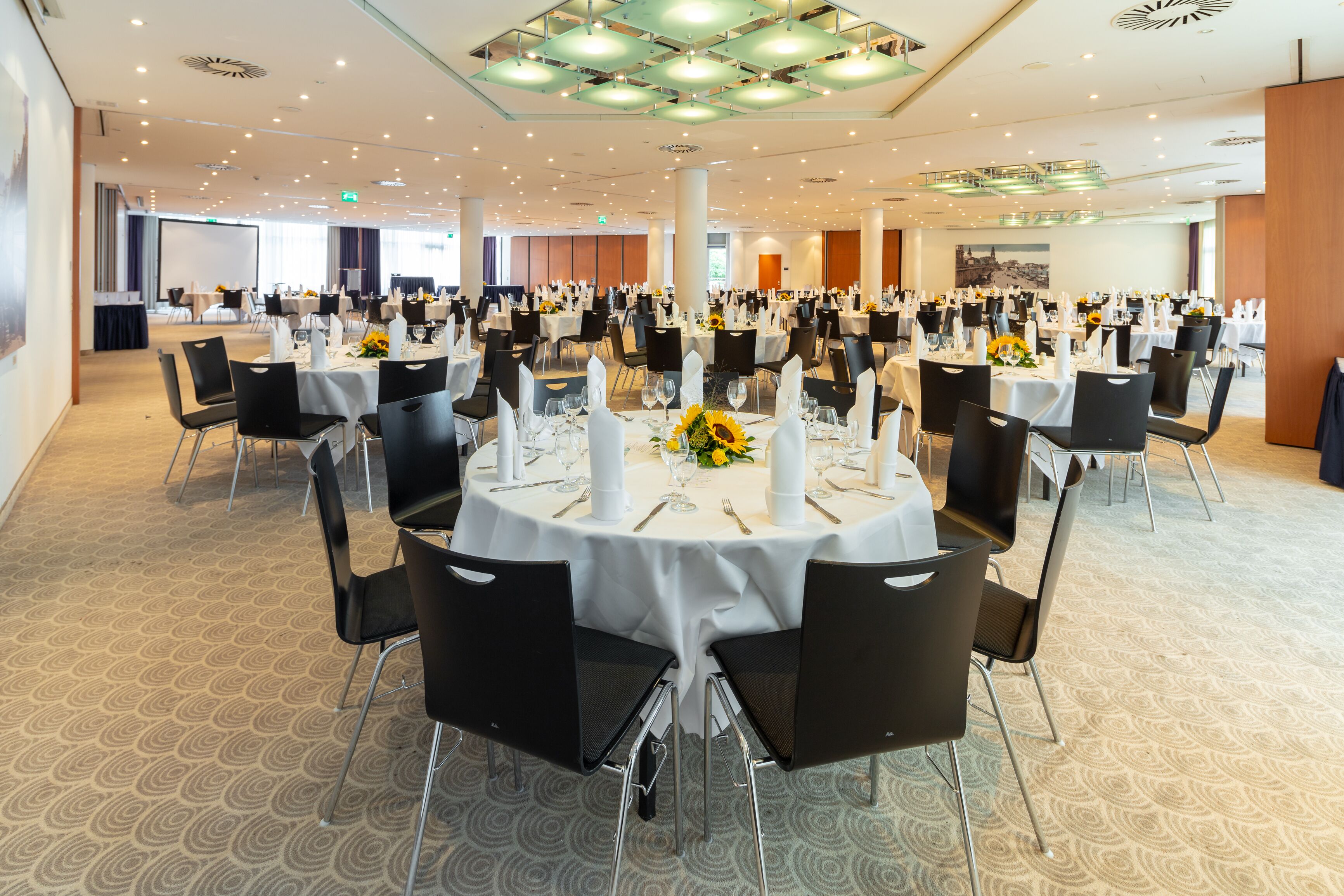 A large banquet hall with round tables set for dining, featuring white tablecloths and black chairs.
