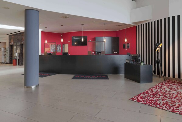 Un área de recepción moderna con una pared de acento roja, un mostrador negro y un pilar grande.