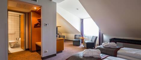 Habitación de hotel con dos camas, un escritorio, una silla, una mesita y un baño.