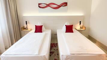 Una habitación de hotel con dos camas individuales, una alfombra con estampado rojo y blanco, un cuadro abstracto rojo y blanco en la pared y lámparas de noche.