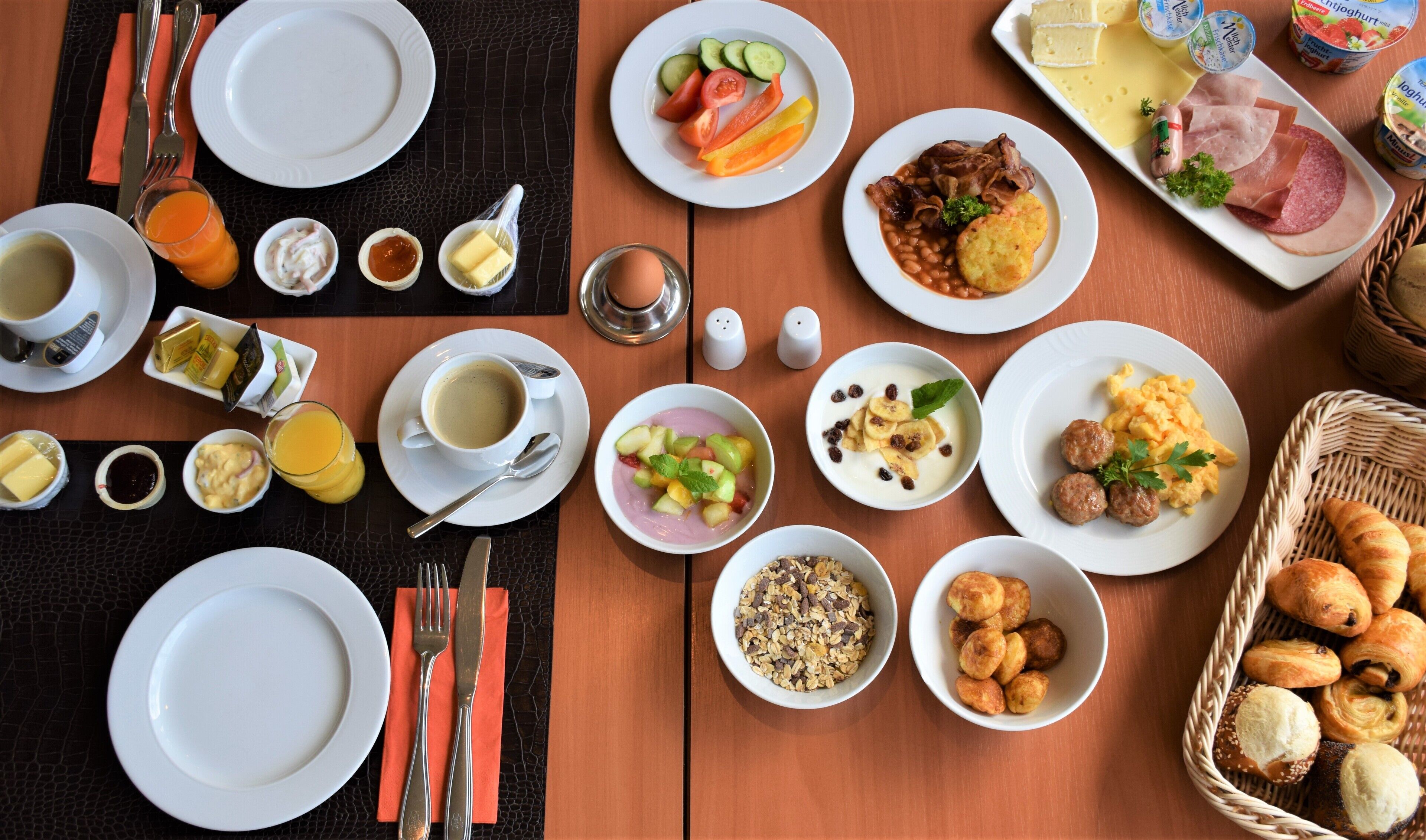 A breakfast buffet with various dishes, including fruits, meats, and pastries, arranged on a wooden table.