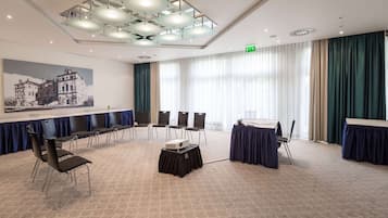Una sala de conferències amb una taula gran, cadires, un projector i una finestra amplia amb cortines.