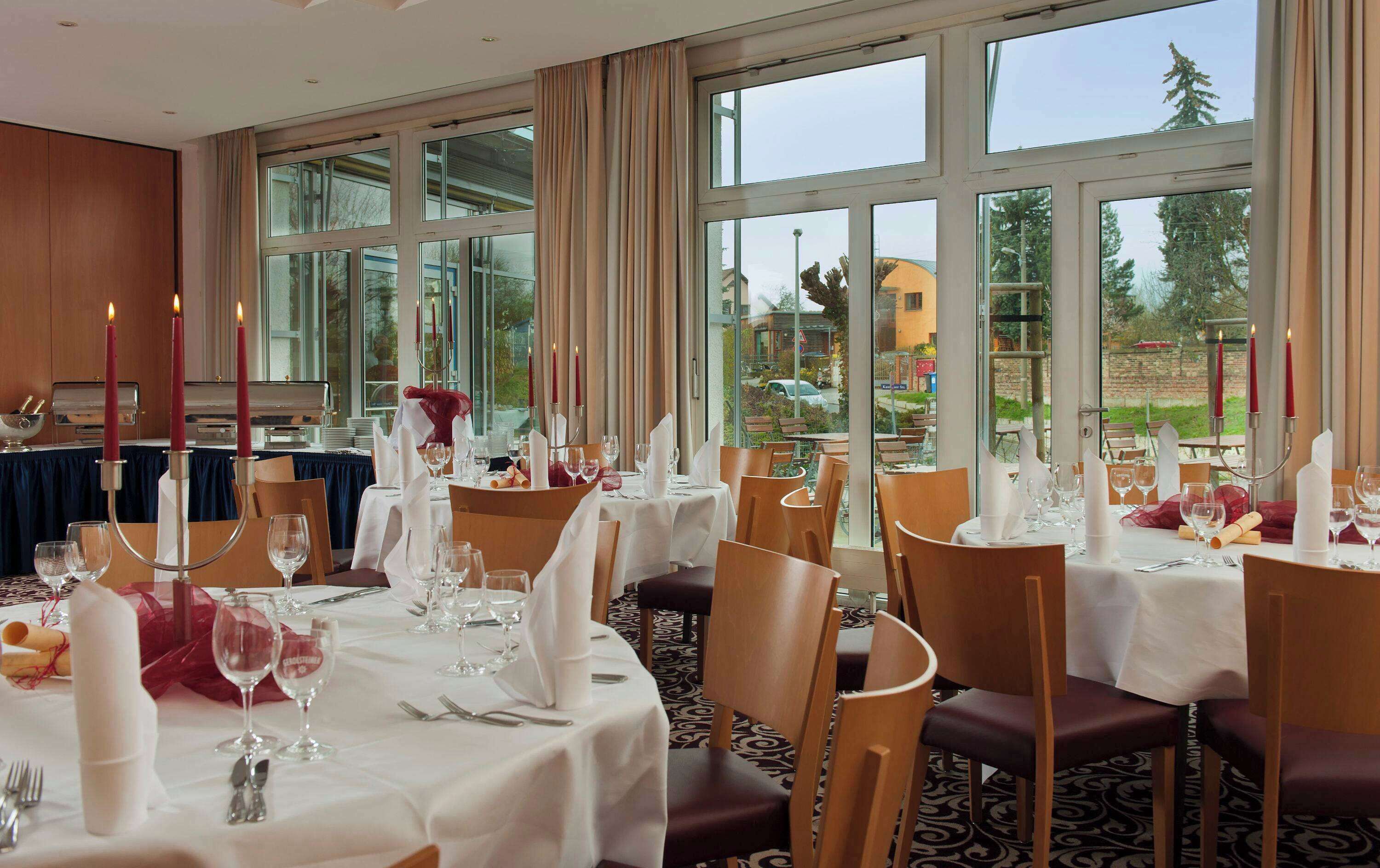 A dining area with tables set for a meal, large windows, and a view of the outdoors.