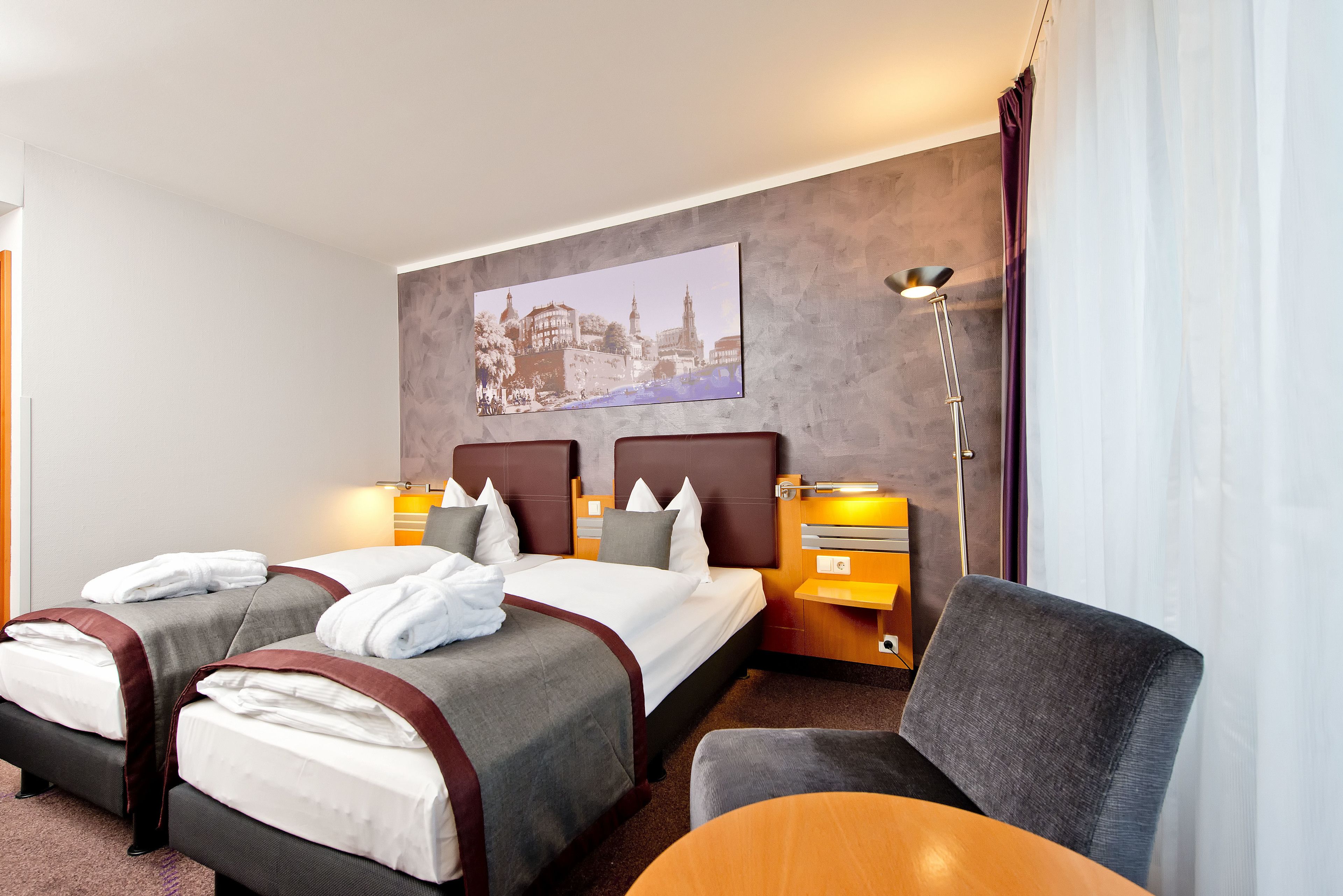 A hotel room with two beds, a desk, a chair, and a large painting on the wall.