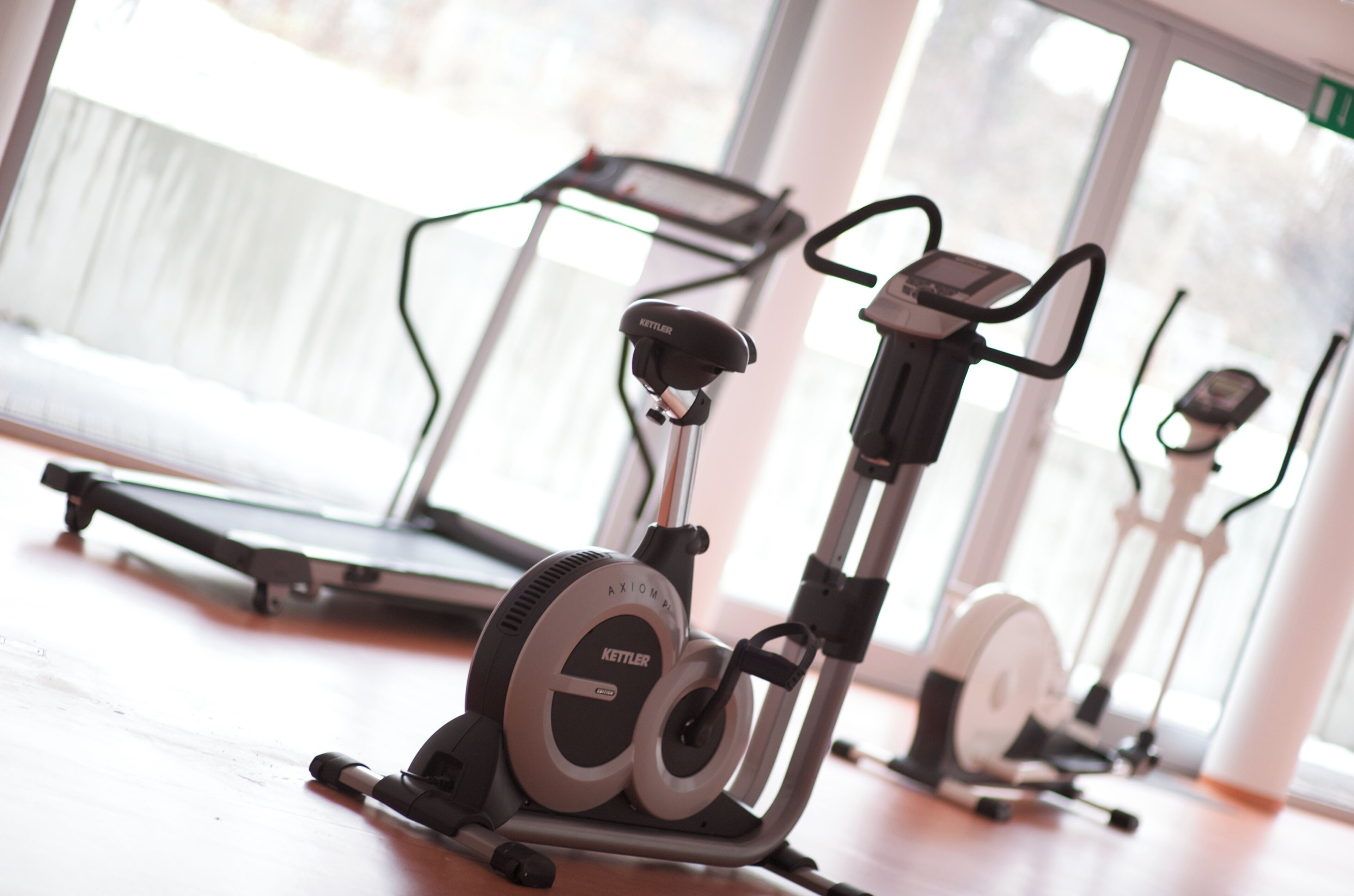 Een fitnessapparaat met een digitaal display, geplaatst in een ruimte met grote ramen en een loopband op de achtergrond.