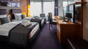 A hotel room with two beds, a desk with a television, a chair, and a view of a cityscape through large windows.