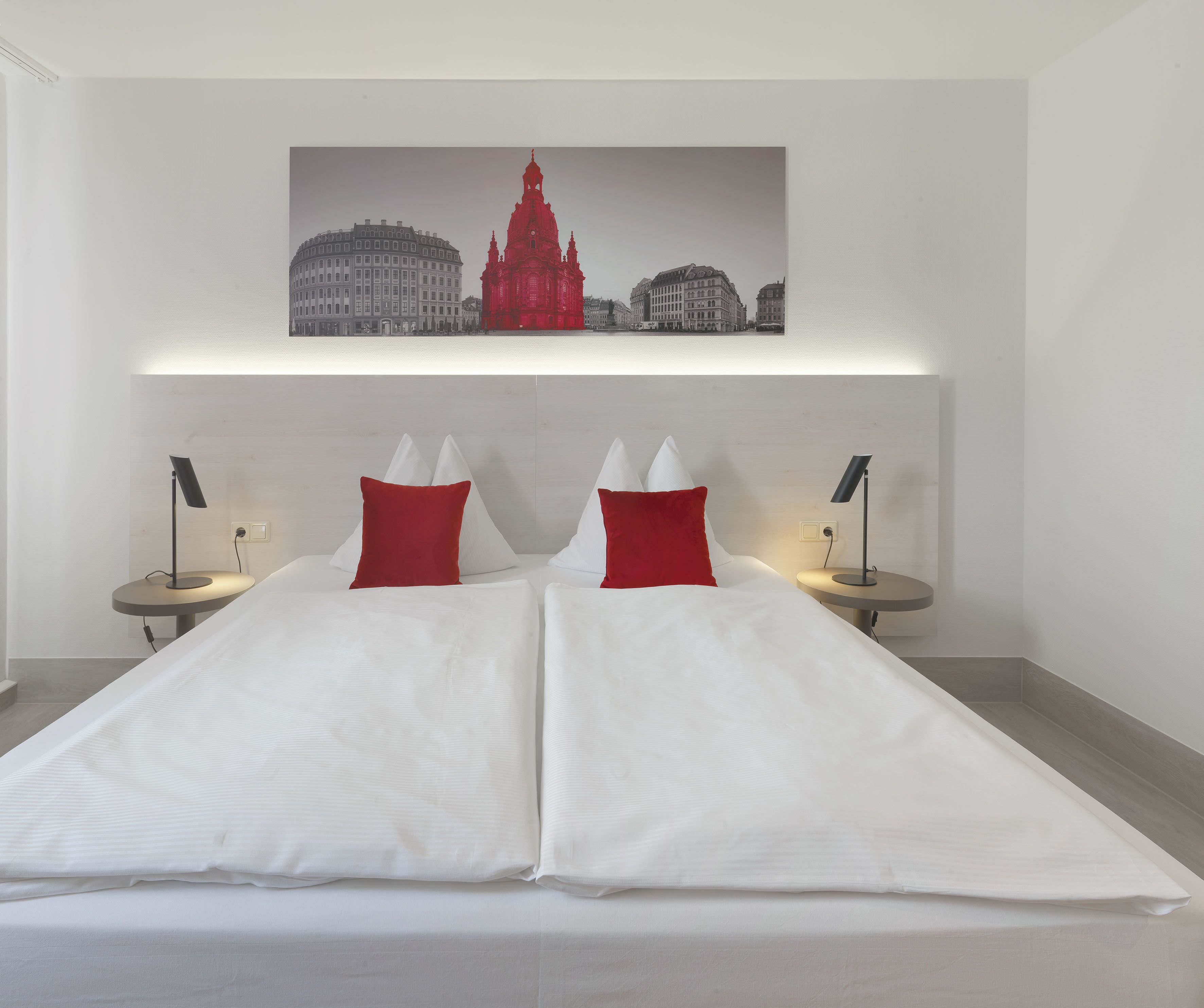 Ein Hotelzimmer mit einem großen Bett, zwei Nachttischen mit Lampen und einem Stadtbild über dem Bett.