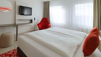 Ein Hotelzimmer mit einem Bett, einem roten Sessel, einem an der Wand montierten Fernseher und einem Fenster mit Vorhängen.