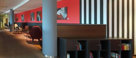 A modern lobby with a red wall, black and white striped wall, and a wooden bookshelf with books.