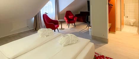 Habitación de hotel con cama, dos sillas rojas, una mesita y un baño visible a través de una puerta abierta.