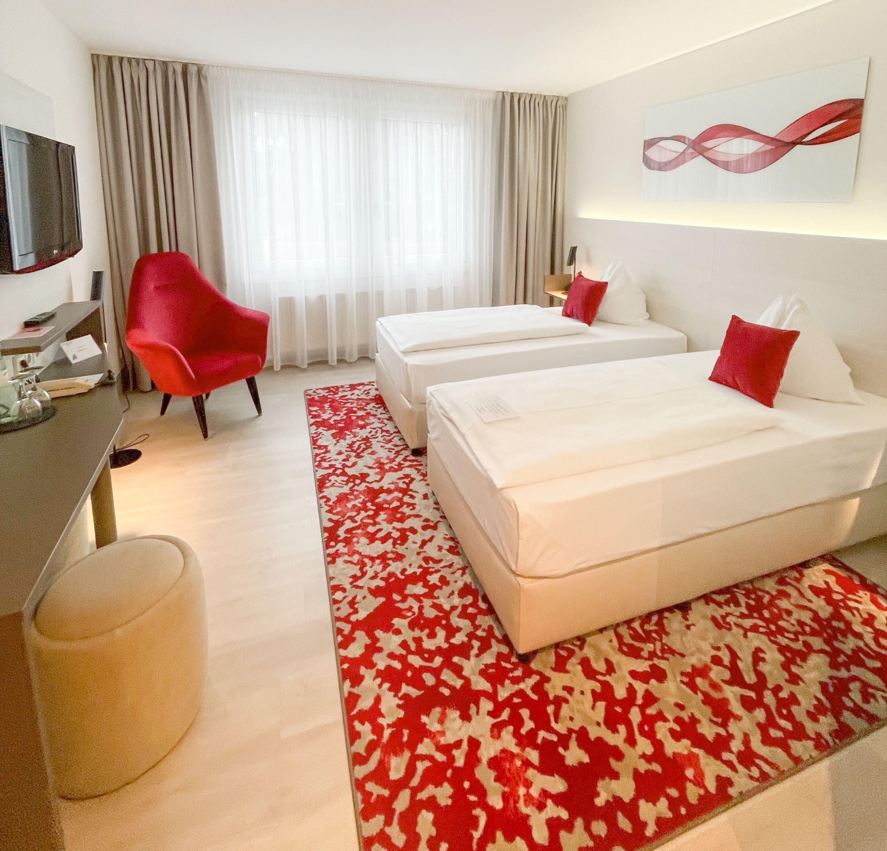 A hotel room with two beds, a red chair, a TV, and a red and white patterned rug.