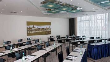 Un salón de conferencias con largas mesas, sillas y botellas de agua.