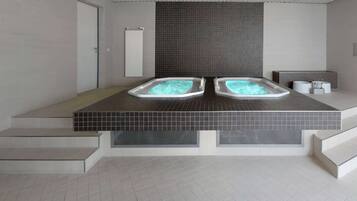 Ein moderner Wellnessbereich mit zwei Whirlpools, einem gefliesten Boden und einer Tür.