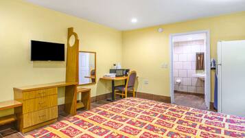 A hotel room with a bed, a desk, a chair, a television, a mirror, and a bathroom visible through an open door.