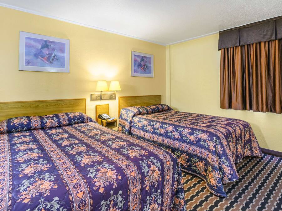 Ein Hotelzimmer mit zwei Betten, jeweils mit blumigem Bettbezug, einem Nachttisch mit Lampe und zwei gerahmten Bildern an den Wänden.