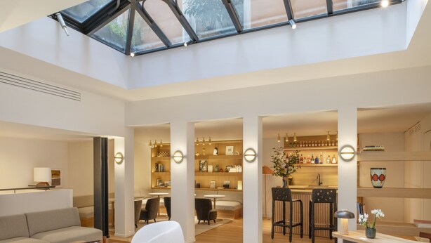 A spacious interior with a high ceiling, a skylight, a seating area with a table, and a kitchen area with bar stools. - Nuage Hôtel (Paris)
