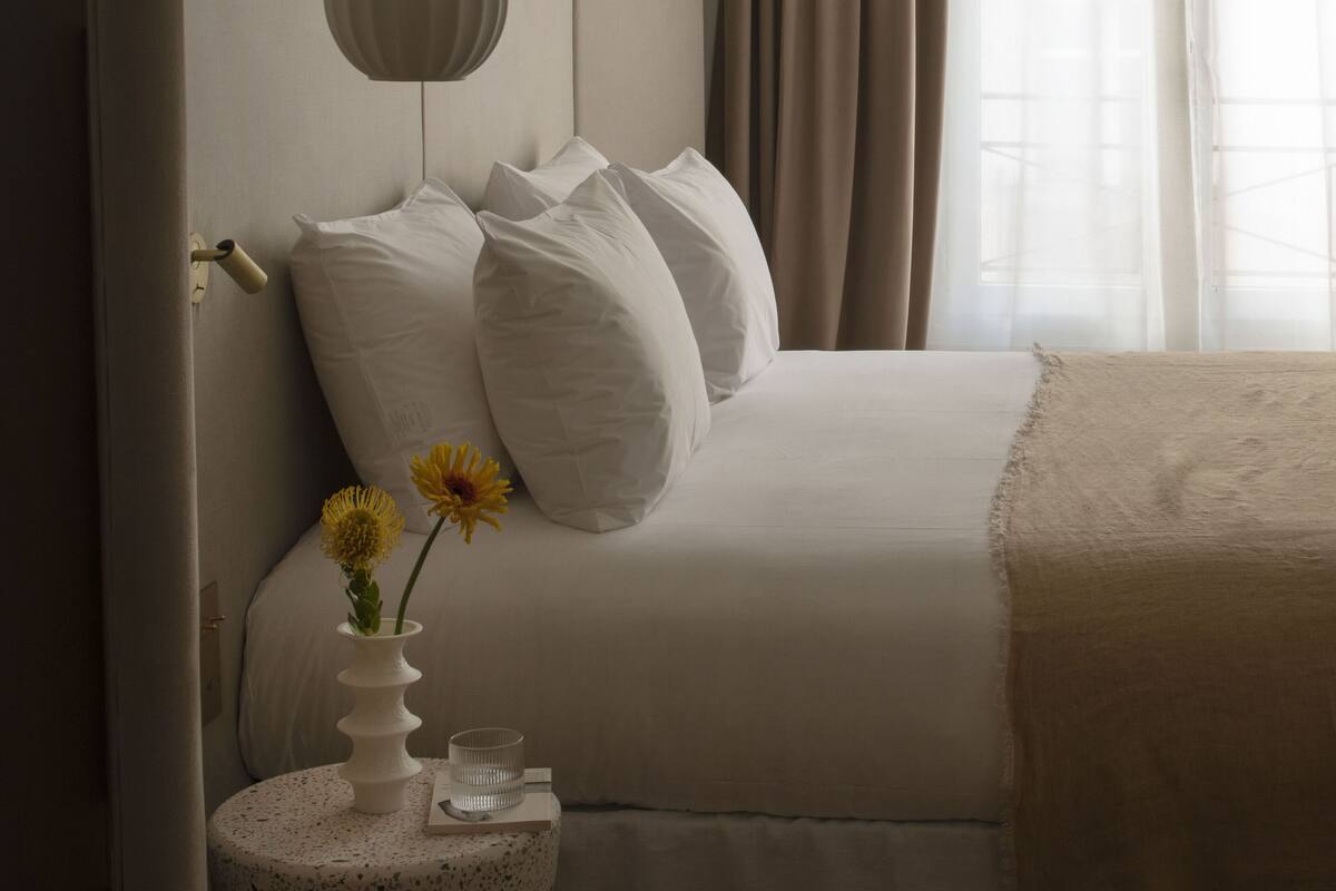 Un dormitorio moderno con una cama grande, una mesita de noche con un florero y velas, y una lámpara colgante.