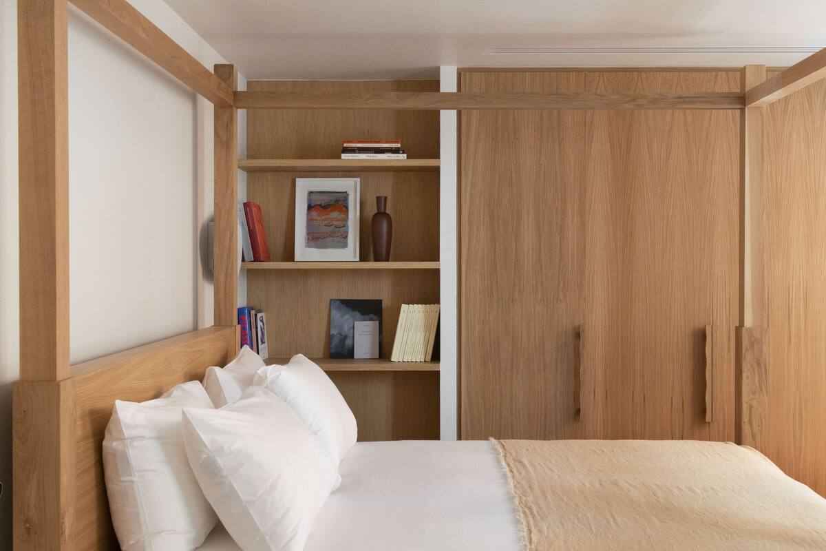 Un dormitorio con estructura de cama de madera, cabecera, mesita de noche y armario empotrado.