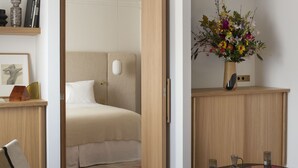 A modern hotel room with a bed, a desk, a chair, a round table with drinks, and a vase with flowers. - Nuage Hôtel (Paris)