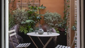 An outdoor patio with a round table and two chairs, surrounded by plants and a wooden fence. - Nuage Hôtel (Paris)