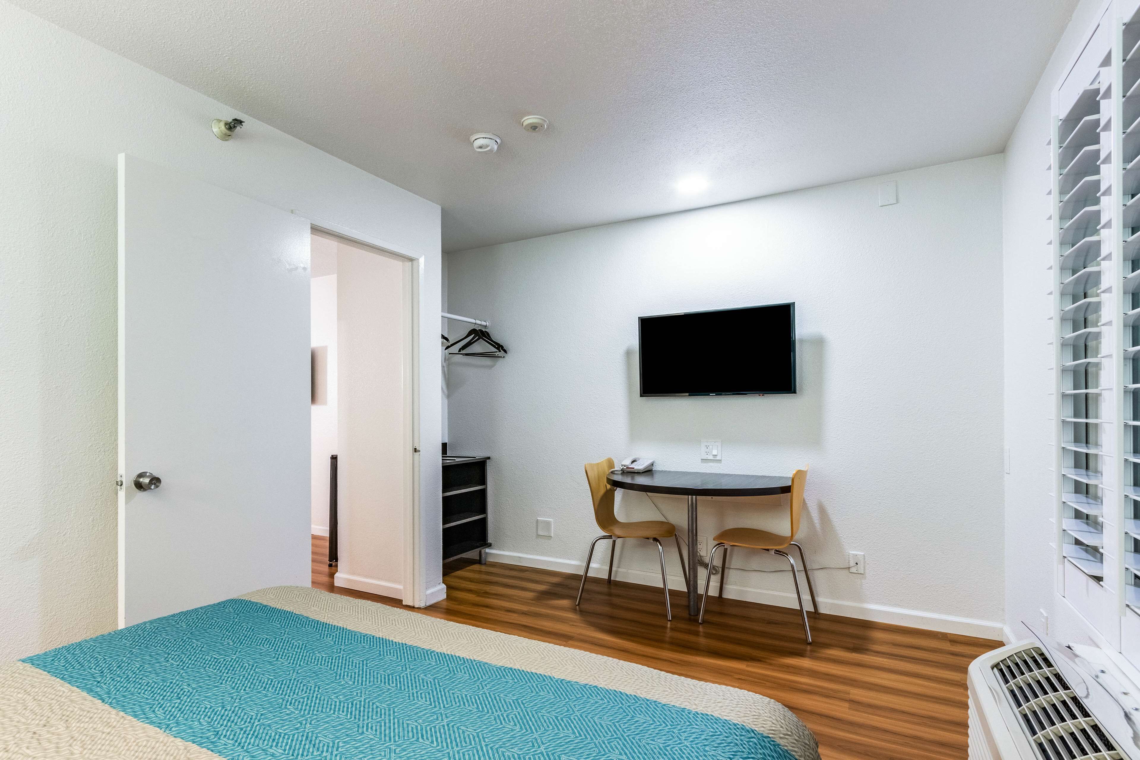 Une petite pièce propre, équipée d’un lit, d’un bureau, d’une chaise, d’un téléviseur et d’un radiateur.