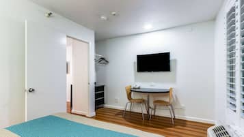 A small, clean room with a bed, a desk, a chair, a TV, and a heater.