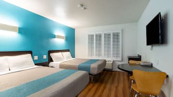 A hotel room with two beds, a TV, a desk with a chair, and a window with blinds.