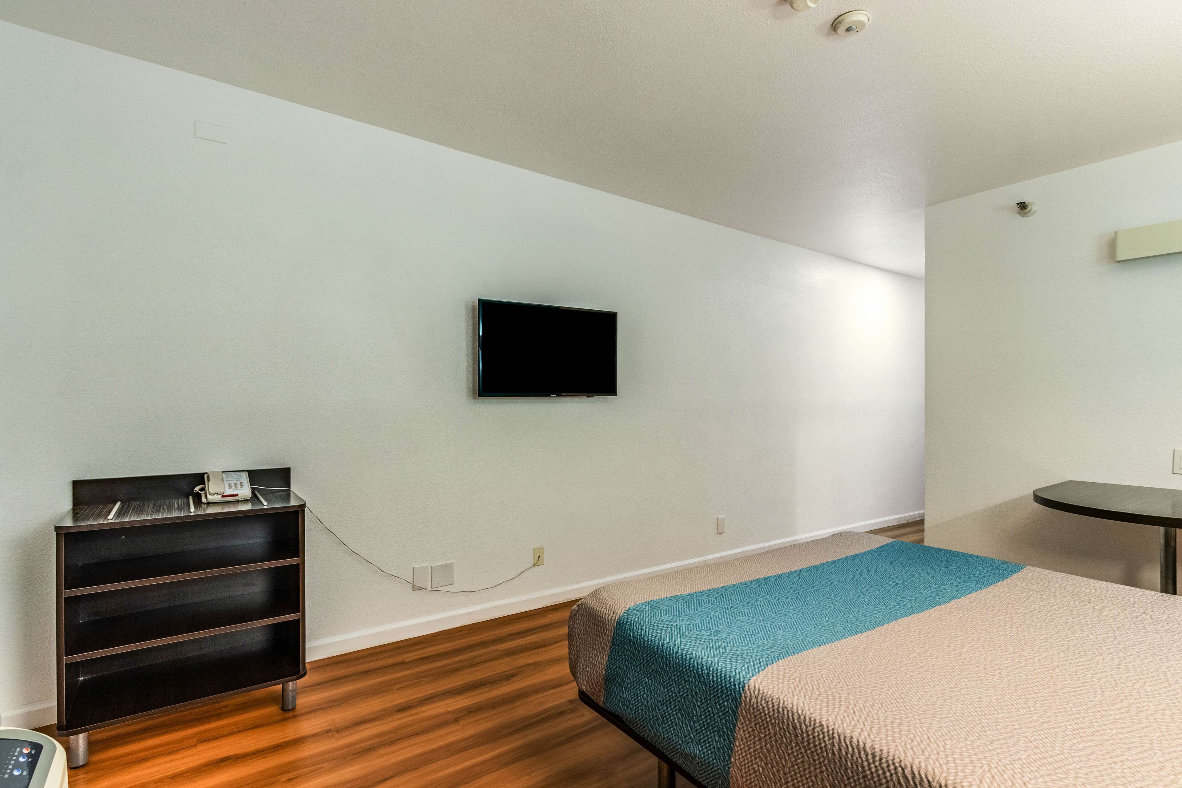 Een hotelkamer met een bed, een aan de muur bevestigde televisie, een klein tafeltje en een houten vloer.