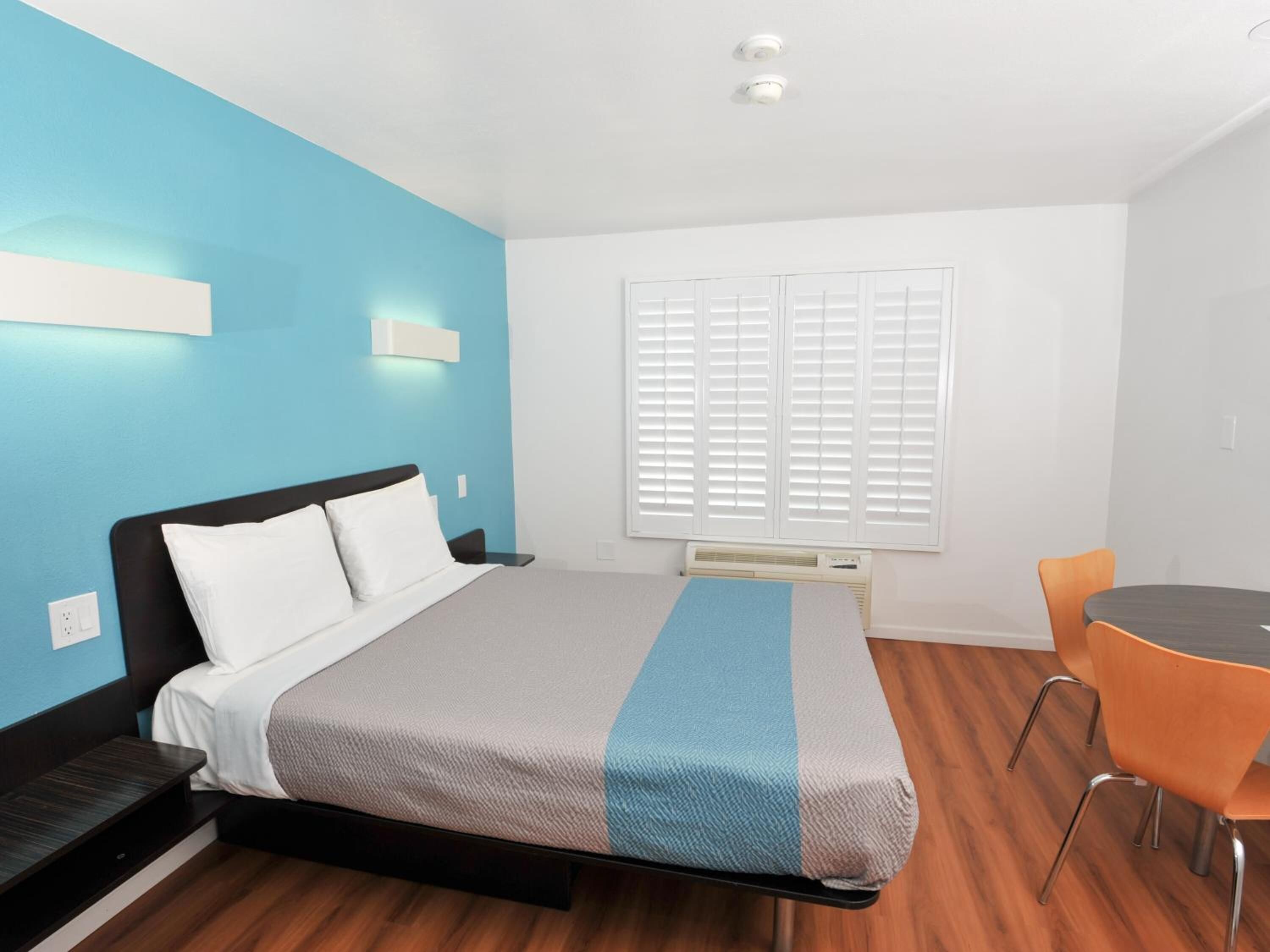 A modern hotel room with a bed, a desk, and a chair.