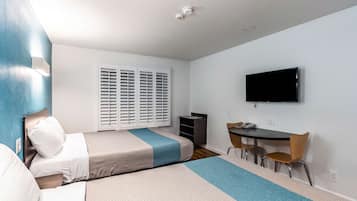 Habitación de hotel con dos camas, un escritorio, una silla, un televisor y una ventana con persianas.