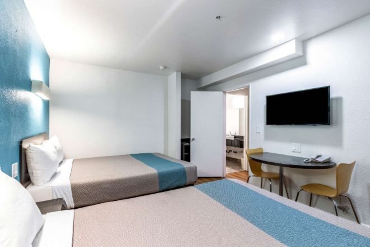 A hotel room with a bed, a desk, a chair, and a TV mounted on the wall.