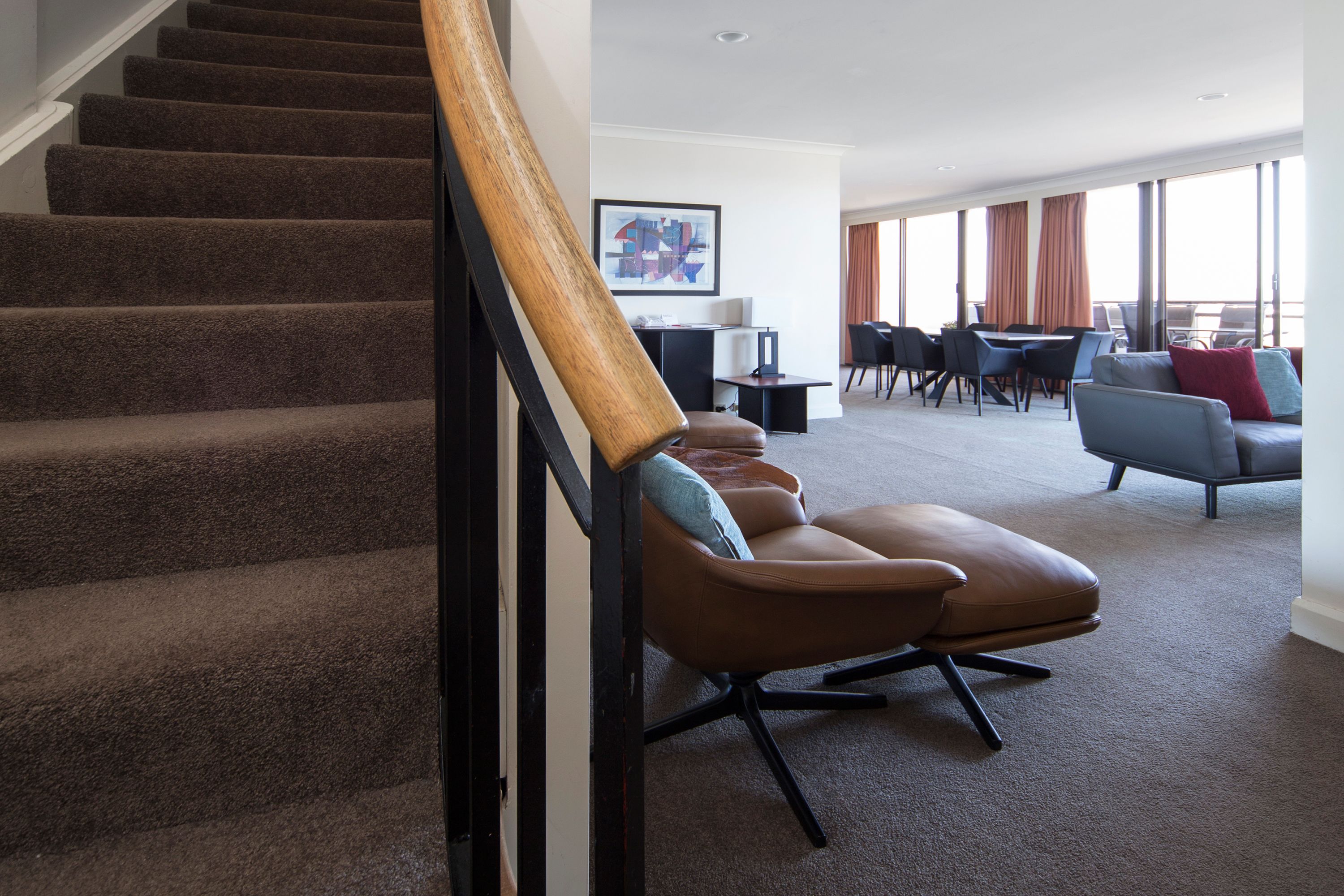 A modern hotel room with a carpeted staircase, a seating area with a sofa and chairs, and large windows offering a view.