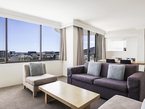 A modern hotel room with a large window offering a city view, a sofa, a chair, and a small table. - BreakFree Capital Tower (Canberra)