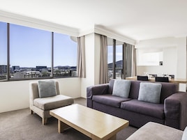 Habitación de hotel moderna con un ventanal grande que ofrece vistas a la ciudad, un sofá, una silla y una mesita.