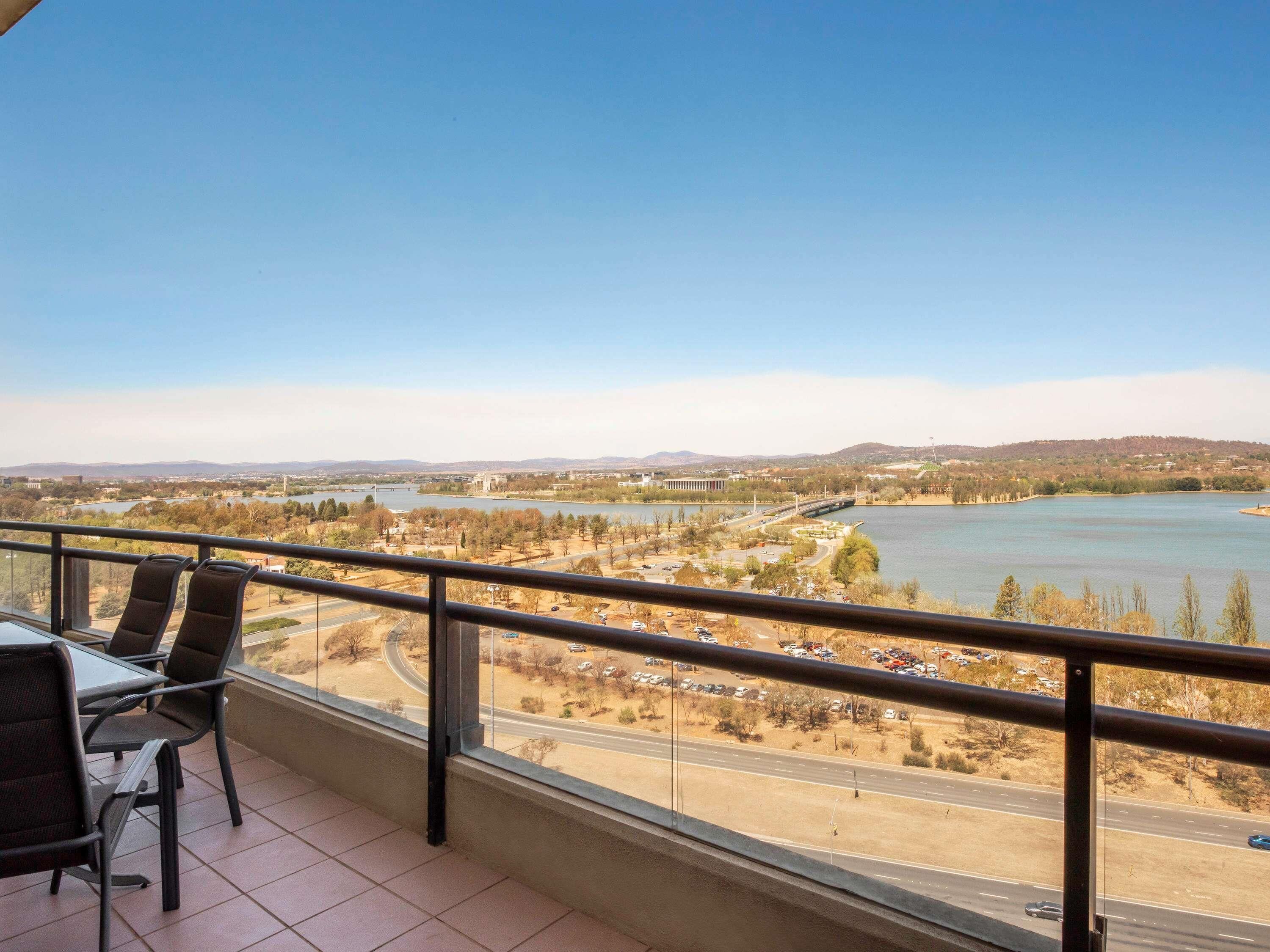 Een balkon met een tafel en stoelen, met uitzicht op een rivier, een brug en verre heuvels.