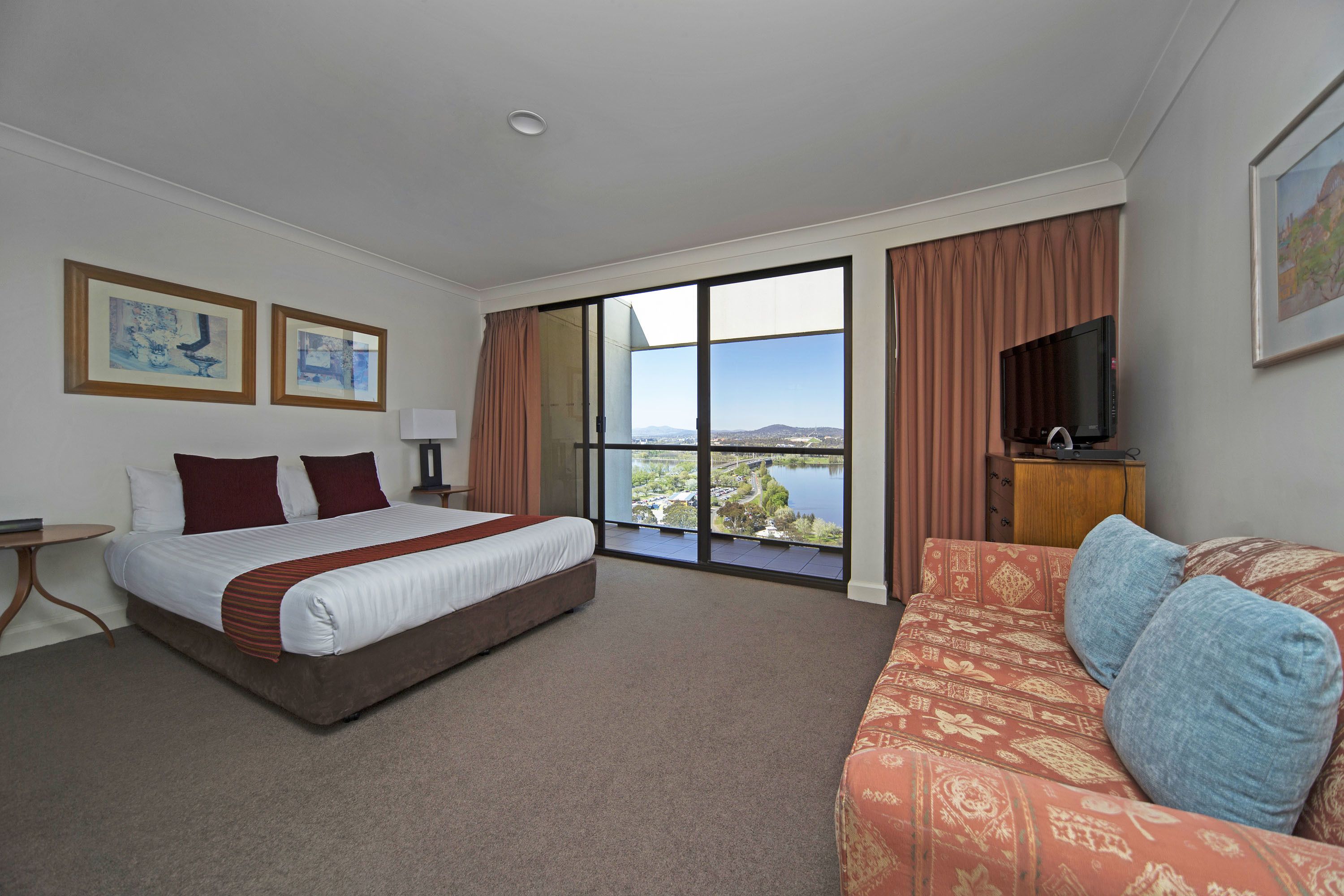 Una habitación de hotel con una cama grande, un sofá, un televisor y vistas a un lago.