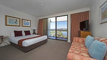 Una habitación de hotel con una cama grande, un sofá, un televisor y vistas a un lago.