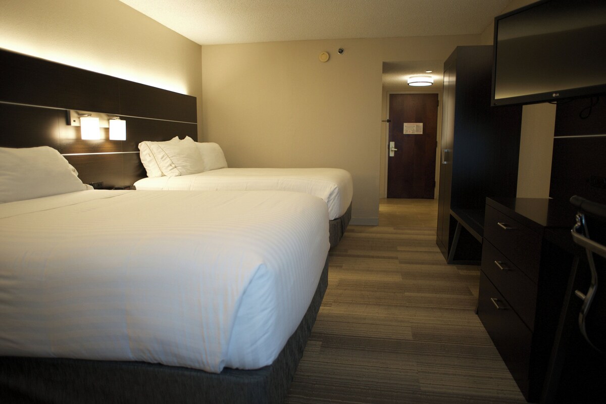 A hotel room with two beds, a TV, and a desk.