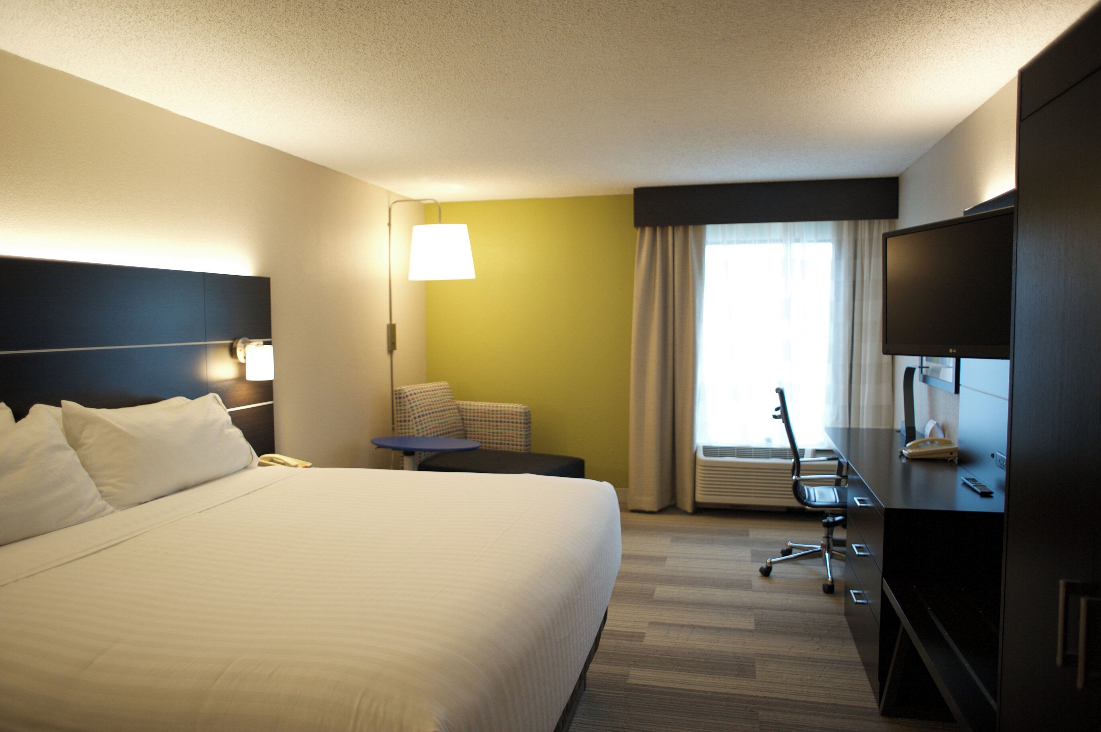 A hotel room with a large bed, a desk with a chair, a television, and a window with curtains.