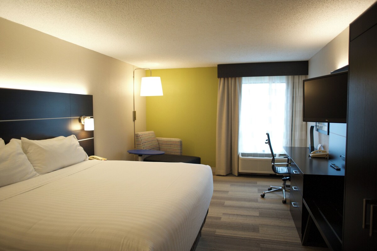 A hotel room with a large bed, a desk with a chair, a television, and a window with curtains.