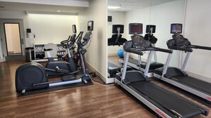 A gym with treadmills, elliptical machines, and a mirrored wall.