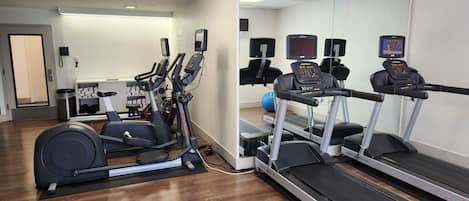 Et fitnesscenter med løbebånd, crosstrainere og en spejlvæg.