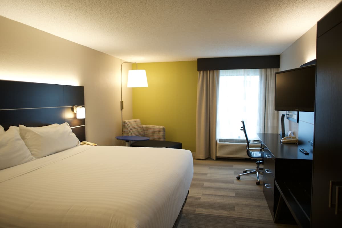 A hotel room with a large bed, a desk with a chair, a television, and a window with curtains.