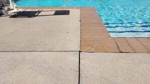 A swimming pool with a slide, a concrete deck, and lounge chairs in the background.