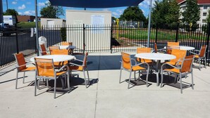 An outdoor patio area with tables and chairs, a covered seating area, and a pool rules sign.