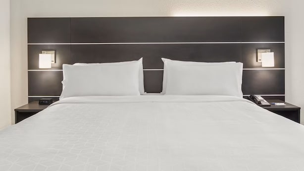 A hotel room with a large bed, two bedside tables, and wall-mounted lighting.