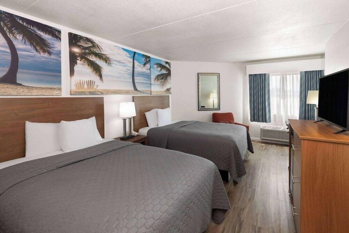 A hotel room with two beds, a desk, a chair, a TV, and artwork on the walls.