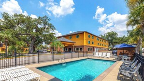 A swimming pool with lounge chairs and a fenced area, surrounded by a building with multiple windows and a palm tree. - Days Inn by Wyndham Biloxi Beach (Biloxi)