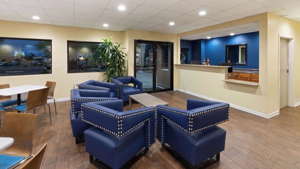 A restaurant with blue upholstered booths, wooden tables, and a large potted plant. - Days Inn by Wyndham Biloxi Beach (Biloxi)
